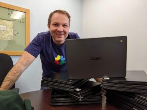John Sowash standing behind a stack of Asus Chromebooks. 